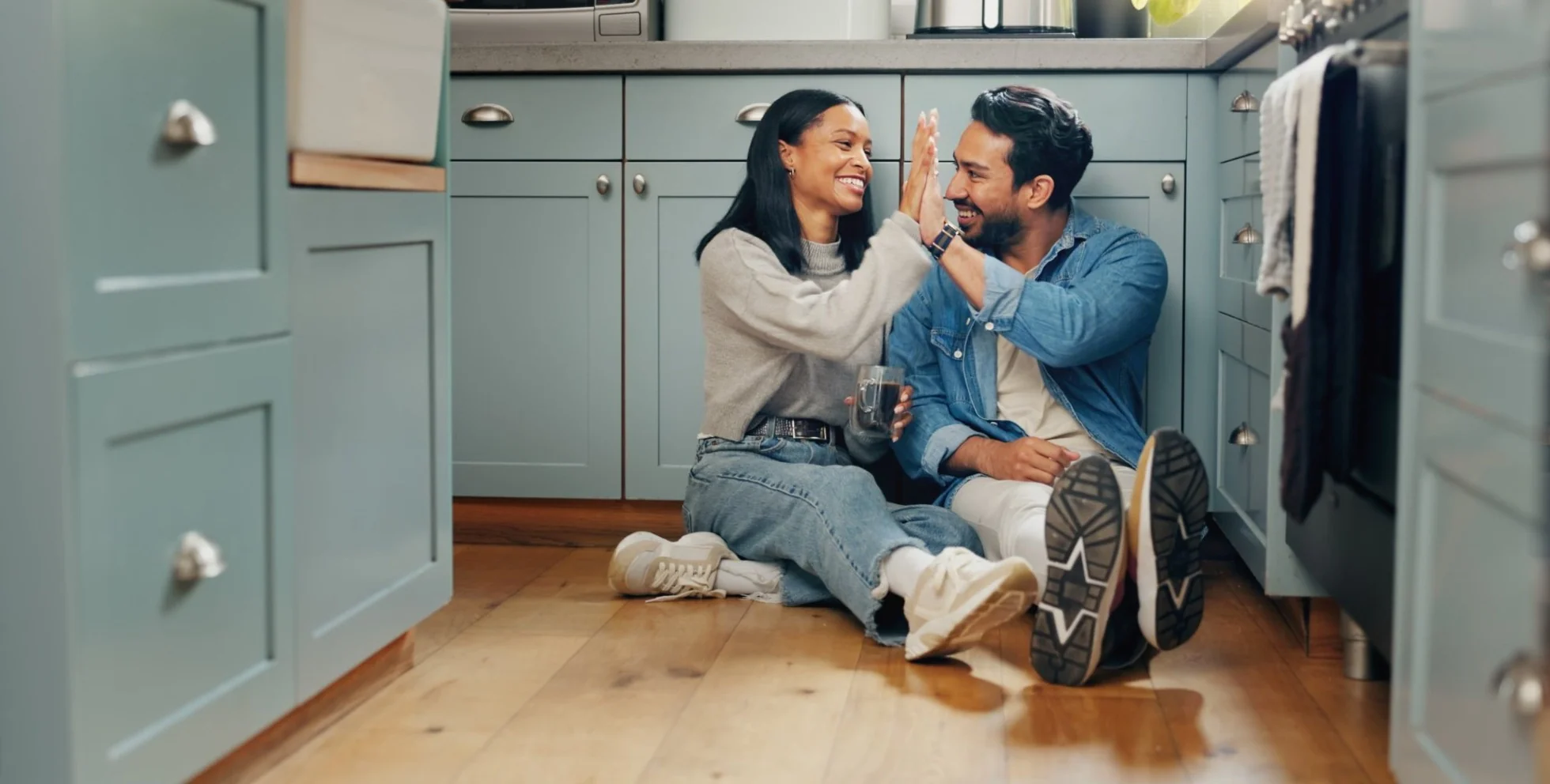 Un couple assis par terre dans sa cuisine se tape dans la main.